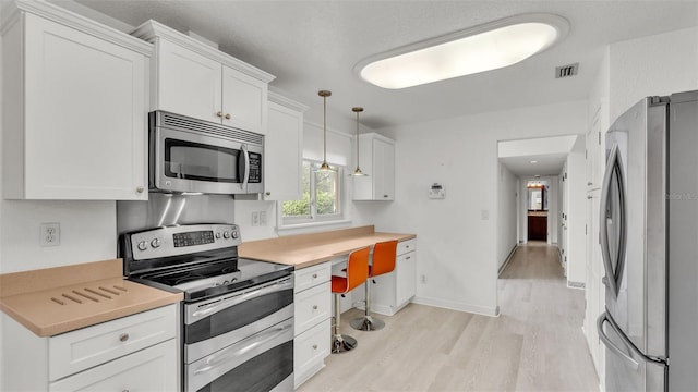 kitchen with white cabinets, pendant lighting, stainless steel appliances, and light hardwood / wood-style flooring