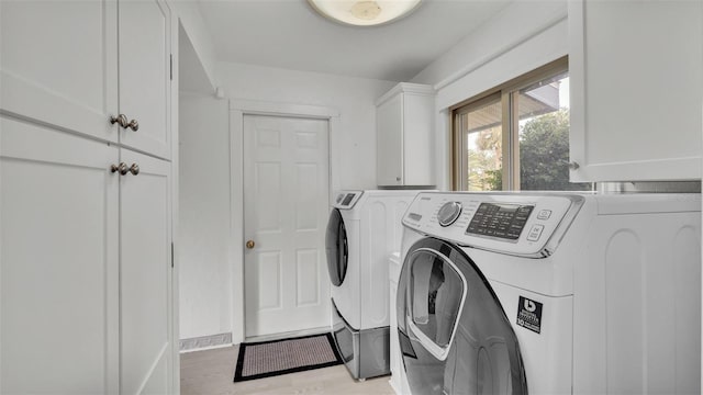 laundry room with cabinets, light hardwood / wood-style floors, and washing machine and clothes dryer