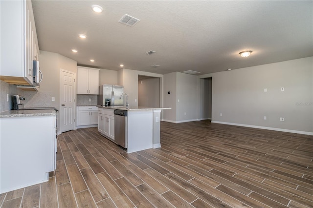 kitchen with appliances with stainless steel finishes, dark hardwood / wood-style flooring, tasteful backsplash, white cabinets, and an island with sink