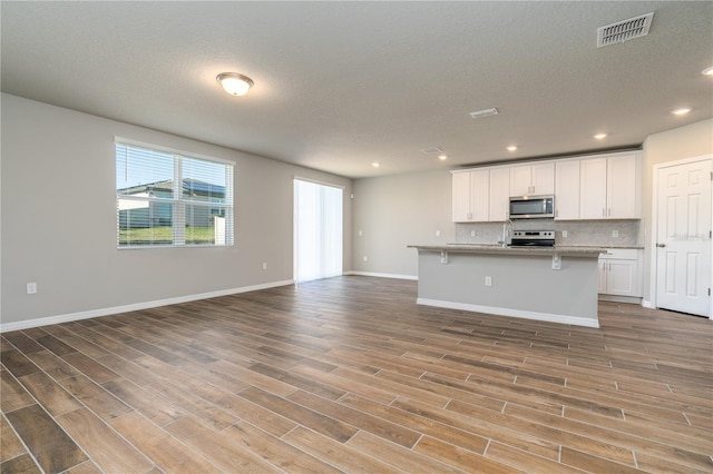 kitchen featuring tasteful backsplash, a kitchen breakfast bar, a kitchen island with sink, white cabinets, and appliances with stainless steel finishes