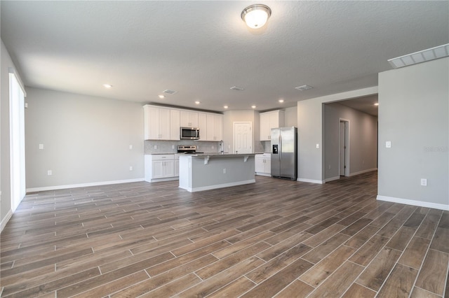 kitchen with stainless steel appliances, dark hardwood / wood-style flooring, decorative backsplash, a center island with sink, and white cabinets