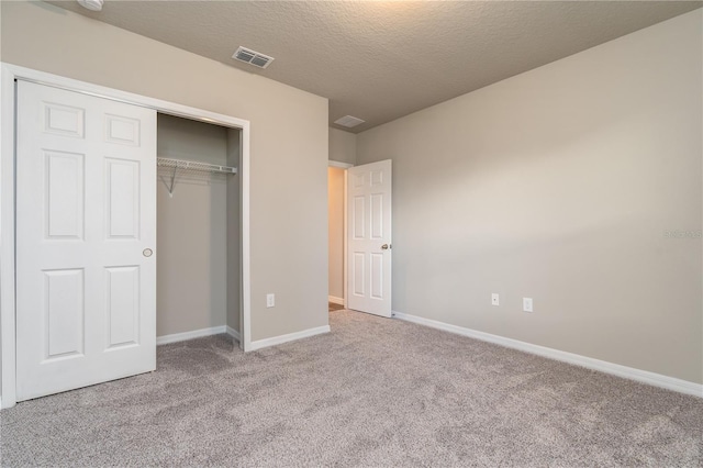 unfurnished bedroom featuring a textured ceiling, light colored carpet, and a closet