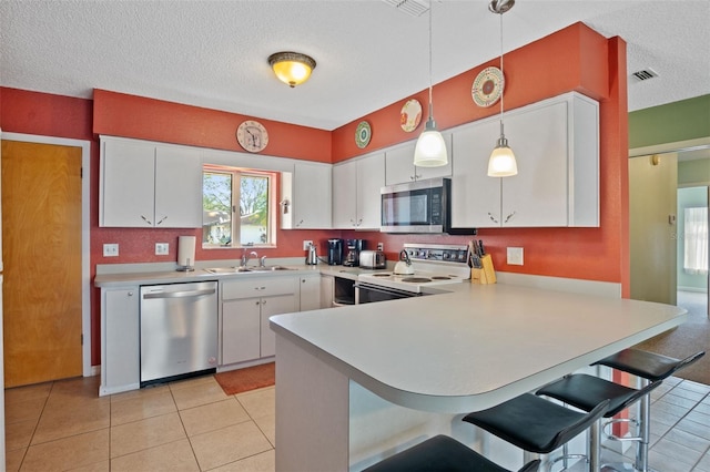 kitchen with light countertops, white cabinets, a peninsula, appliances with stainless steel finishes, and a sink