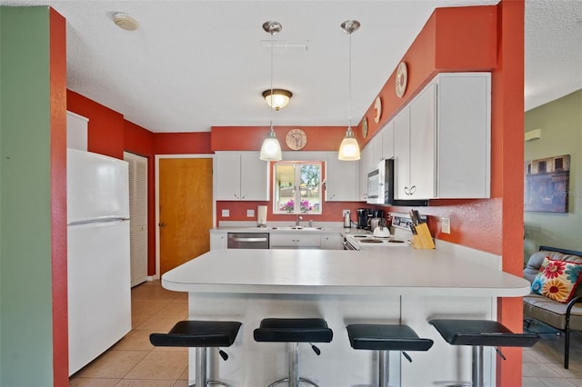 kitchen with white cabinetry, light countertops, white appliances, a sink, and a peninsula