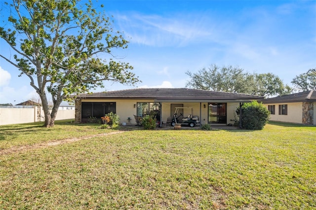 back of house with stucco siding, fence, and a lawn