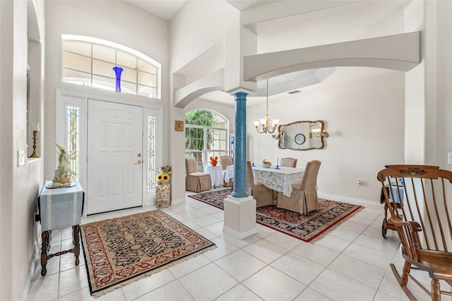 foyer featuring decorative columns, a towering ceiling, light tile patterned floors, and an inviting chandelier