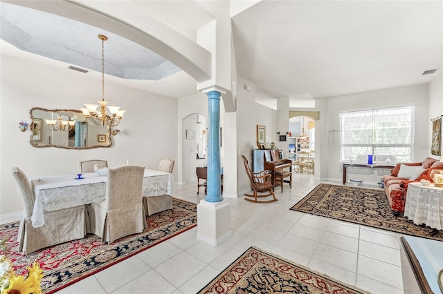 tiled dining space featuring a raised ceiling, ornate columns, and an inviting chandelier