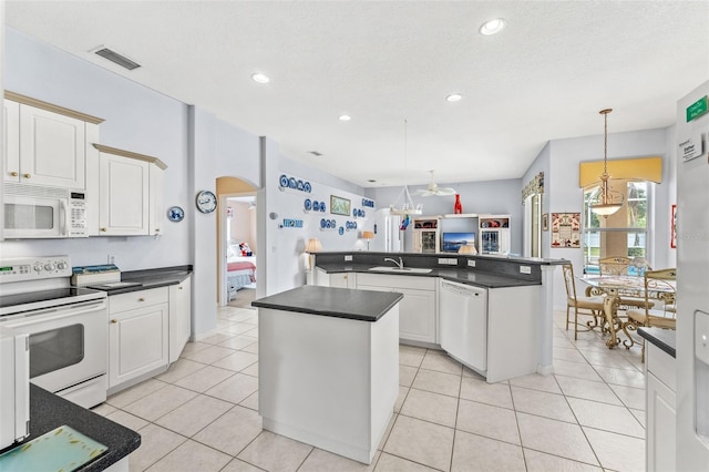 kitchen featuring white appliances, sink, white cabinets, a center island, and hanging light fixtures