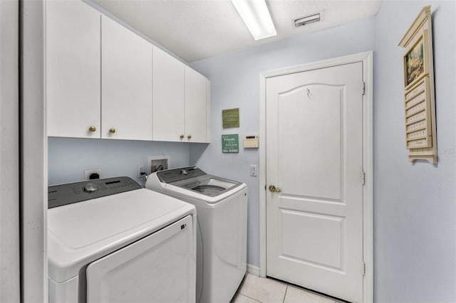 washroom featuring washing machine and clothes dryer, light tile patterned floors, and cabinets