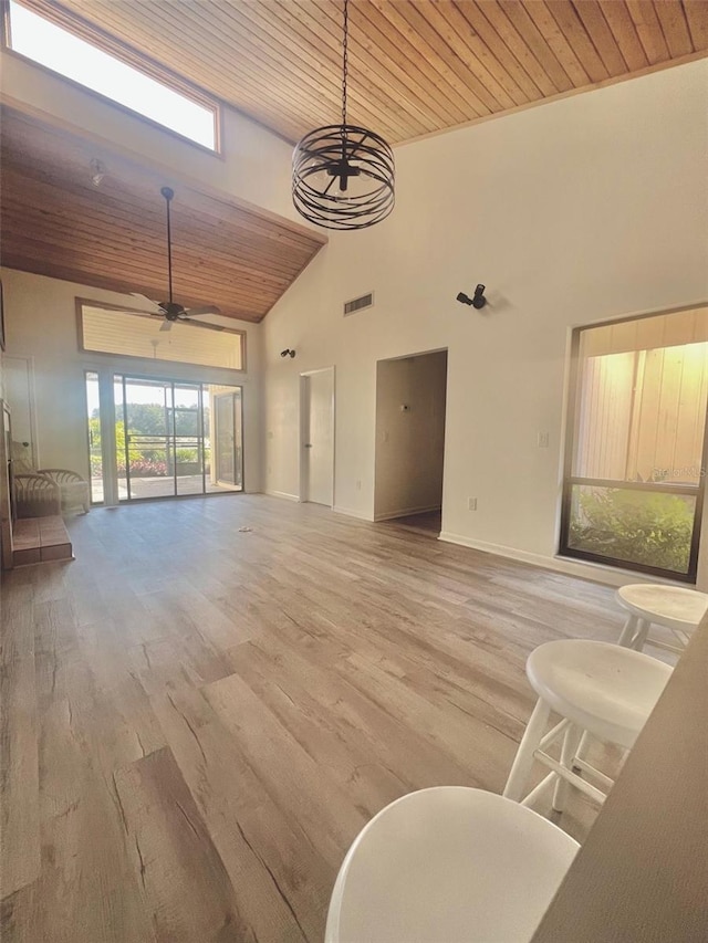 unfurnished living room featuring ceiling fan with notable chandelier, light hardwood / wood-style floors, wood ceiling, and a towering ceiling