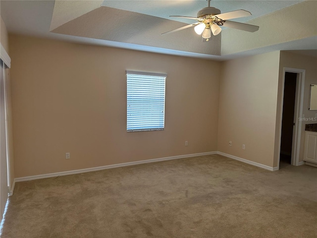 unfurnished bedroom with ceiling fan, a raised ceiling, and light carpet