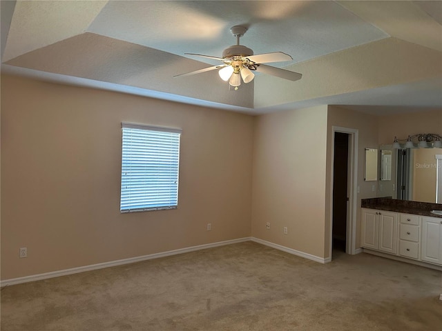 unfurnished bedroom with ceiling fan, a raised ceiling, and light colored carpet