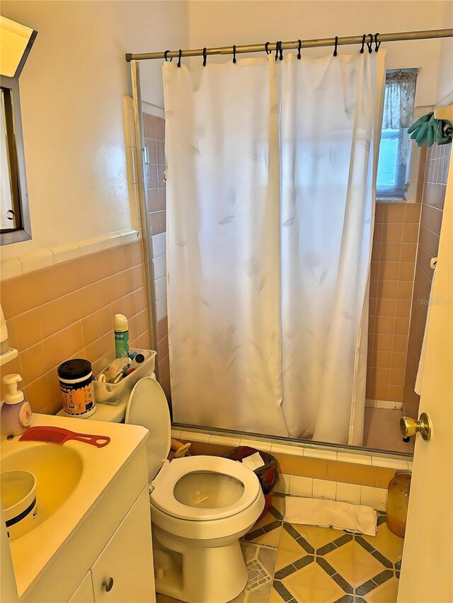 bathroom with walk in shower, tile patterned floors, toilet, tile walls, and vanity