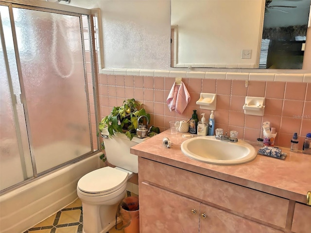 full bathroom with vanity, combined bath / shower with glass door, tile walls, and toilet