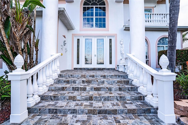 entrance to property featuring a porch, a balcony, and french doors