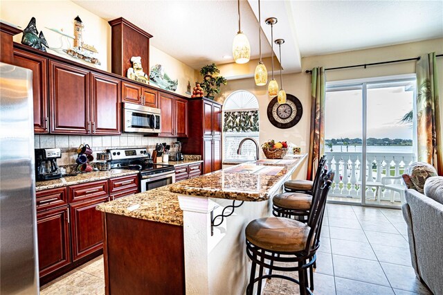 kitchen featuring backsplash, a water view, light stone countertops, an island with sink, and appliances with stainless steel finishes