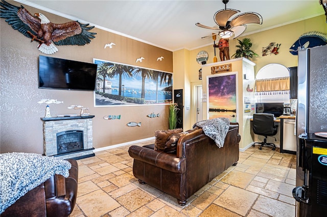 living room featuring ceiling fan, a stone fireplace, and ornamental molding