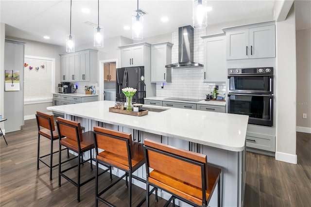 kitchen with multiple ovens, stainless steel fridge with ice dispenser, pendant lighting, and wall chimney range hood