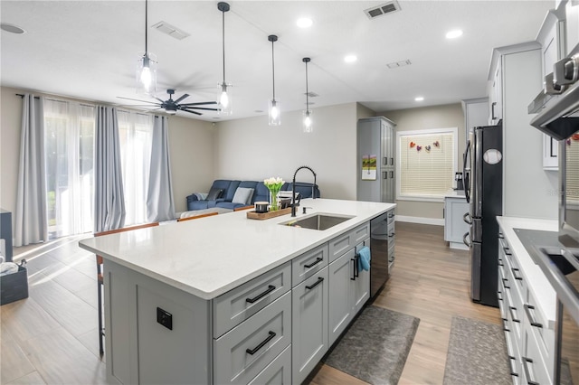 kitchen featuring a kitchen island with sink, sink, stainless steel refrigerator, hanging light fixtures, and a breakfast bar area