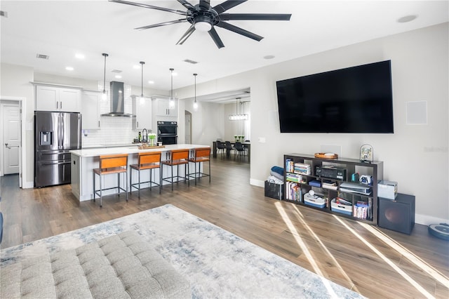 kitchen featuring a breakfast bar, white cabinets, wall chimney range hood, stainless steel fridge, and a large island