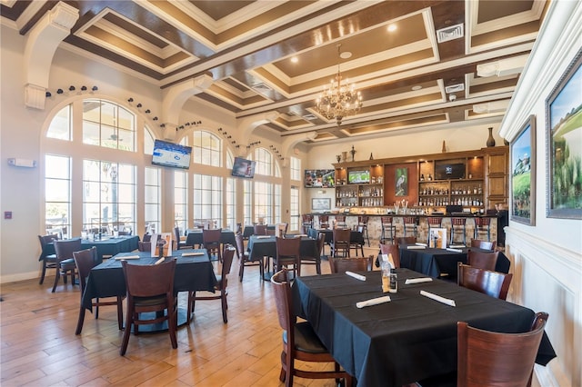 dining space featuring a towering ceiling, ornamental molding, hardwood / wood-style floors, a notable chandelier, and bar area