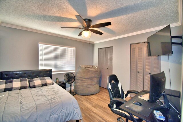 bedroom with ornamental molding, a textured ceiling, ceiling fan, light hardwood / wood-style flooring, and multiple closets