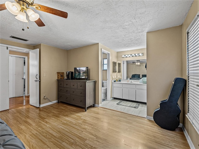 bedroom featuring ensuite bathroom, sink, ceiling fan, light wood-type flooring, and a textured ceiling