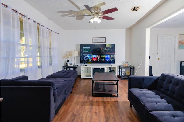 living room with a textured ceiling, ceiling fan, and dark wood-type flooring