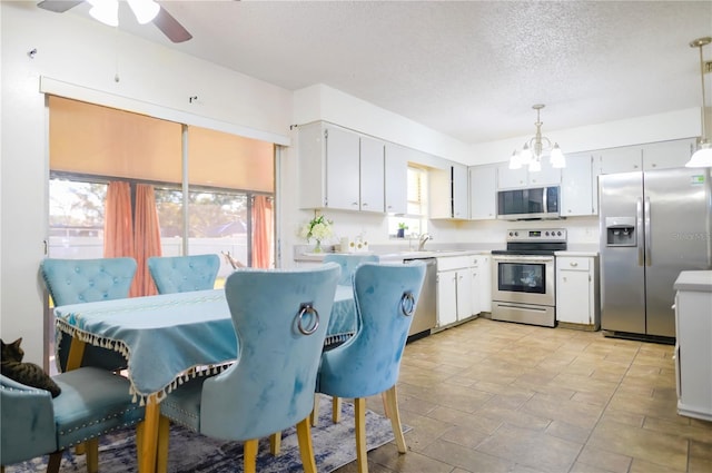 kitchen with appliances with stainless steel finishes, ceiling fan with notable chandelier, a textured ceiling, decorative light fixtures, and white cabinets