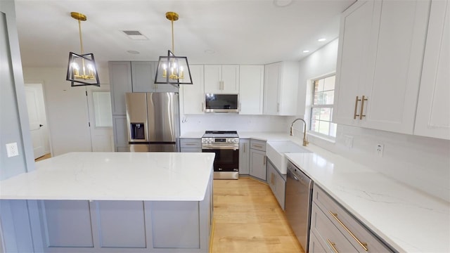 kitchen with light stone countertops, gray cabinetry, stainless steel appliances, sink, and decorative light fixtures