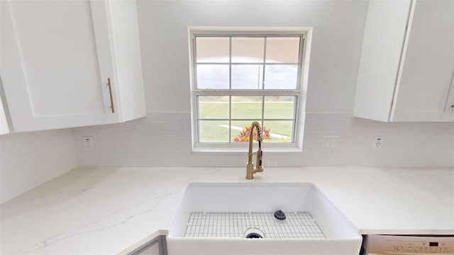 interior details with backsplash, white cabinetry, sink, and light stone countertops