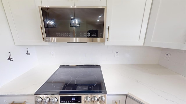 interior details featuring white cabinets, stove, light stone countertops, and tasteful backsplash