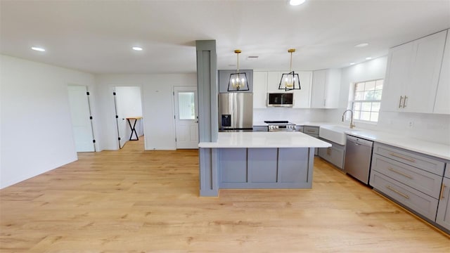 kitchen with gray cabinetry, a center island, sink, hanging light fixtures, and stainless steel appliances