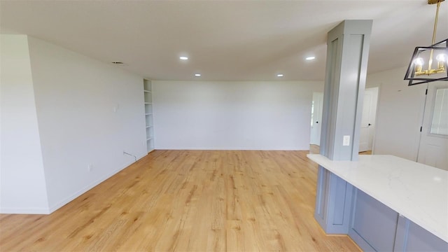 empty room featuring built in shelves, light wood-type flooring, and a chandelier