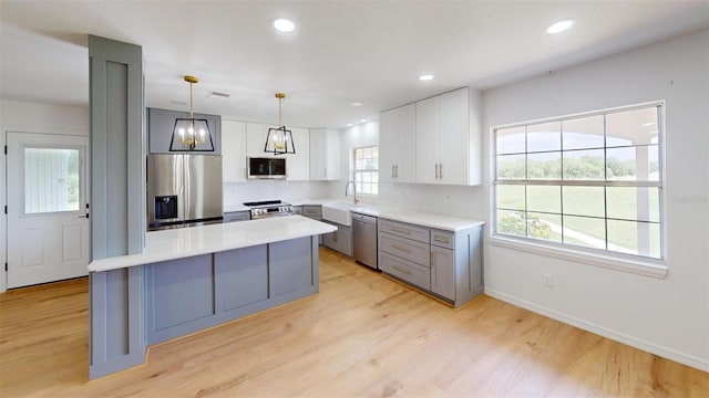 kitchen featuring pendant lighting, a center island, white cabinets, light wood-type flooring, and stainless steel appliances