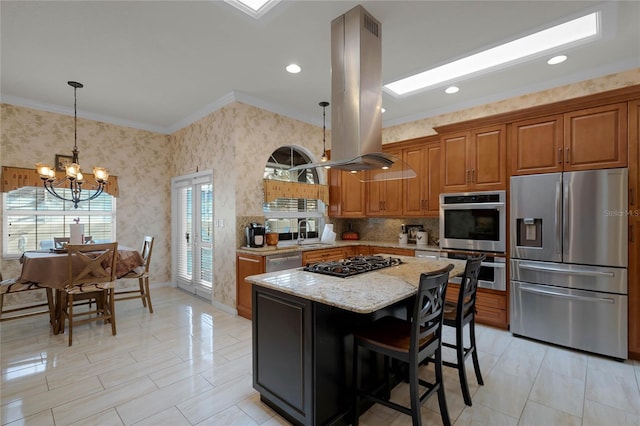 kitchen with island exhaust hood, appliances with stainless steel finishes, a notable chandelier, light stone counters, and a center island