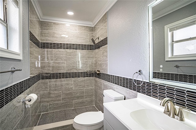 bathroom featuring crown molding, tiled shower, toilet, vanity, and tile walls