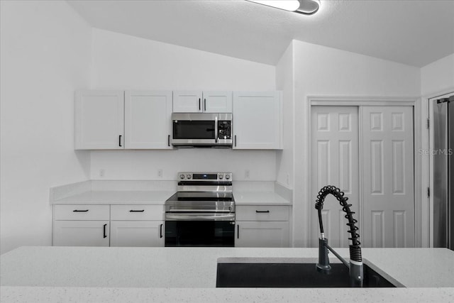 kitchen featuring white cabinetry, sink, appliances with stainless steel finishes, and vaulted ceiling