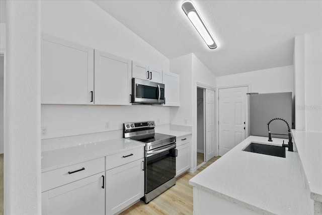 kitchen with white cabinets, stainless steel appliances, lofted ceiling, and sink