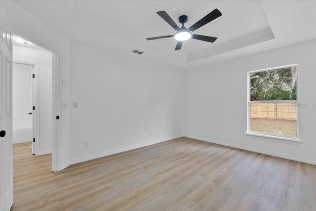 unfurnished room with a raised ceiling, ceiling fan, and light hardwood / wood-style floors