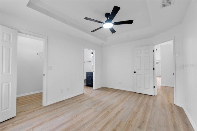 unfurnished bedroom featuring connected bathroom, ceiling fan, a tray ceiling, a walk in closet, and a closet