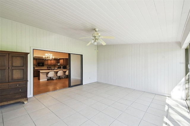 interior space with ceiling fan with notable chandelier, light tile patterned floors, and wood walls