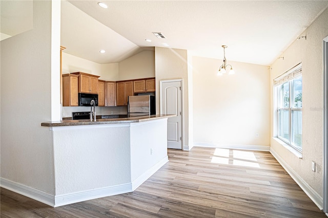 kitchen featuring lofted ceiling, stainless steel fridge, hanging light fixtures, kitchen peninsula, and light wood-type flooring