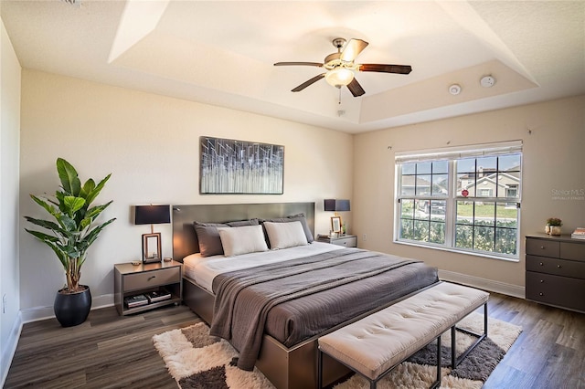 bedroom with dark hardwood / wood-style floors, ceiling fan, and a tray ceiling