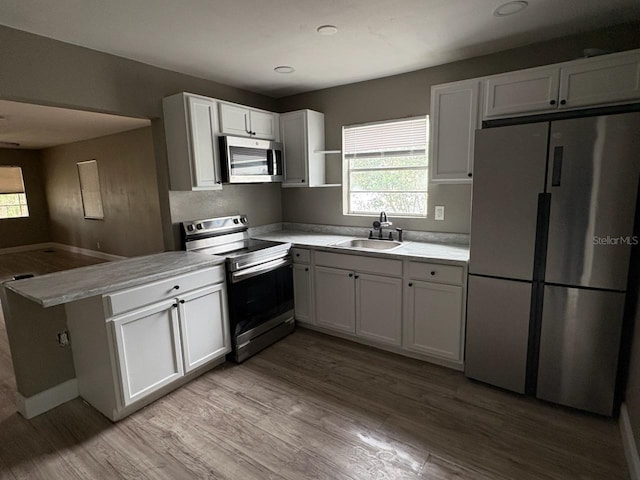 kitchen featuring white cabinets, sink, light hardwood / wood-style flooring, appliances with stainless steel finishes, and kitchen peninsula