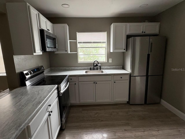 kitchen with white cabinets, sink, appliances with stainless steel finishes, and hardwood / wood-style floors