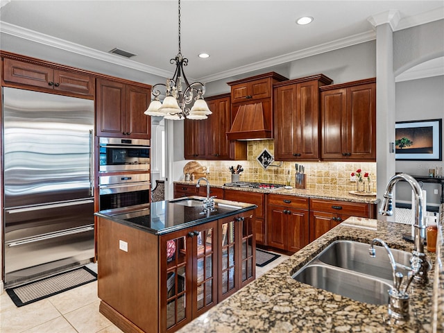 kitchen featuring stainless steel appliances, sink, a kitchen island with sink, and dark stone counters