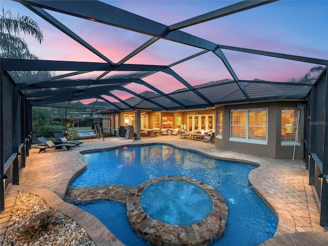 pool at dusk with an outdoor living space, an in ground hot tub, glass enclosure, and a patio