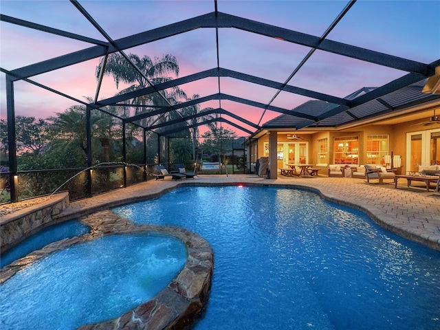 pool at dusk featuring a patio area, a lanai, an in ground hot tub, ceiling fan, and an outdoor hangout area