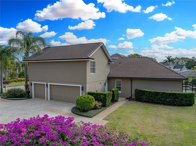 exterior space featuring decorative driveway, a tile roof, a yard, and stucco siding